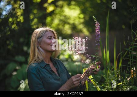 Donna matura che tocca la pianta fiorita in giardino Foto Stock