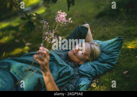 Donna matura contemplativa sdraiata in giardino Foto Stock