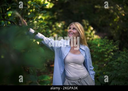 Donna matura che tocca la pianta in giardino Foto Stock