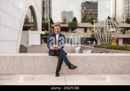 Buon uomo d'affari messaggi di testo sullo smartphone al parcheggio ufficio Foto Stock