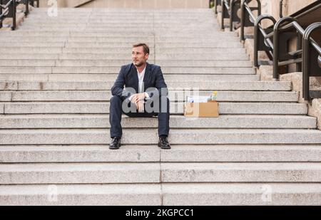 Triste uomo d'affari seduto con scatola di cartone sulle scale Foto Stock