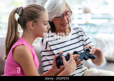 Nonna e nipote che parlano tra loro tenendo joystick a casa Foto Stock