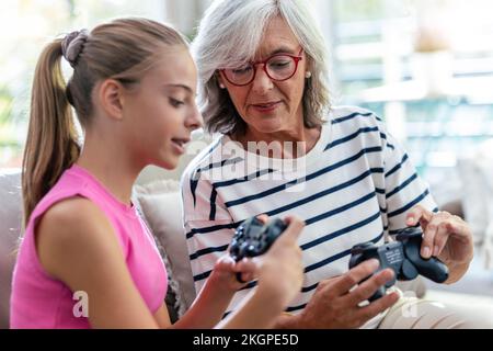 Nonna insegna a nonna di usare il joystick per giocare a videogame a casa Foto Stock