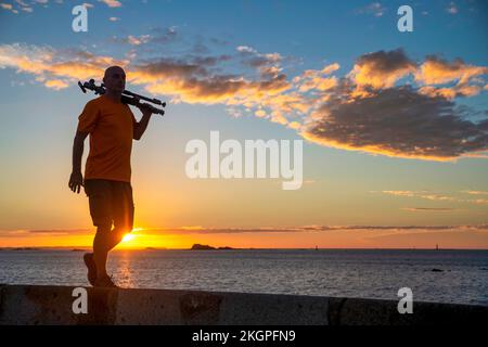 Uomo maturo che cammina con il cavalletto sul molo al tramonto Foto Stock