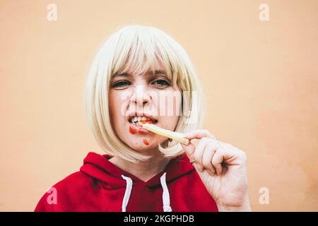 Donna che mangia patatine fritte con ketchup di fronte alla parete della pesca Foto Stock