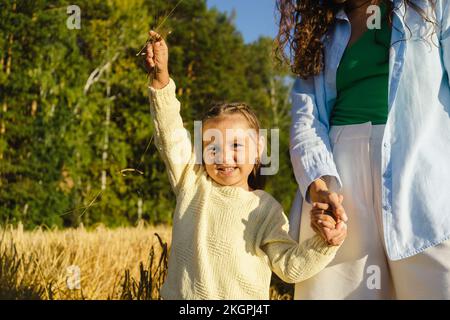 Ragazza che tiene le mani con la madre e che sta in piedi sul campo il giorno di sole Foto Stock