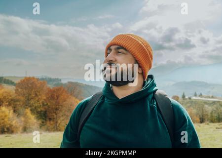 Uomo sorridente che indossa un cappello a maglia arancione con zaino Foto Stock