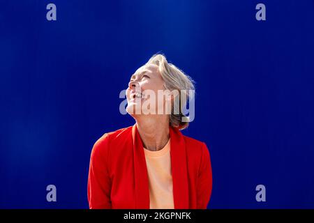 Donna felice con blazer rosso di fronte al muro blu Foto Stock