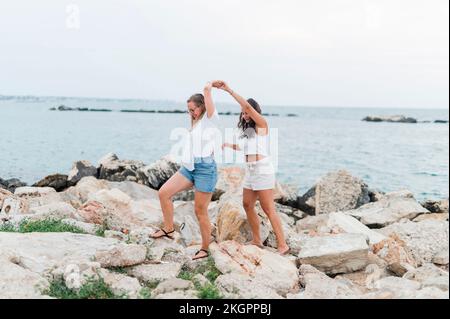 Amici che tengono le mani e camminano insieme sulla roccia in spiaggia Foto Stock