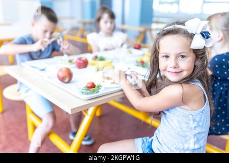 Ragazza sorridente che pranzerà con gli amici seduti al tavolo nella caffetteria della scuola Foto Stock