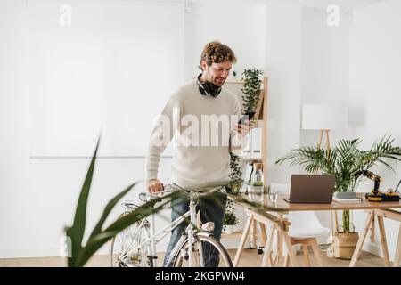 Uomo d'affari con messaggi di testo in bicicletta sullo smartphone sul posto di lavoro Foto Stock