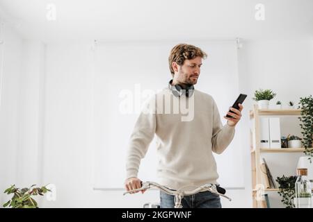 Uomo d'affari con la bicicletta che usa lo smartphone sul posto di lavoro Foto Stock