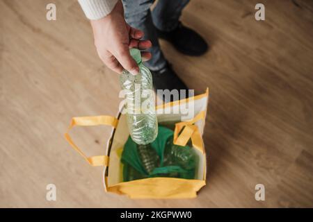 Uomo d'affari che getta una bottiglia di plastica nel sacchetto in ufficio Foto Stock