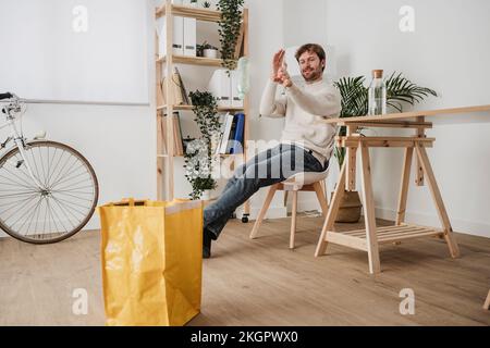 Uomo d'affari che getta la bottiglia di plastica nel sacchetto giallo sul posto di lavoro Foto Stock