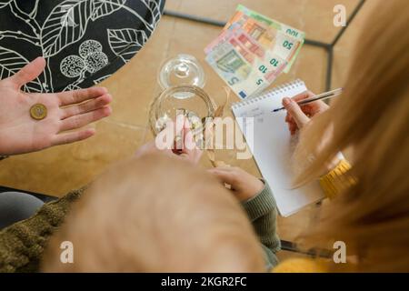 Mano dell'uomo che tiene la moneta con la donna che scrive sul blocco note nel paese Foto Stock