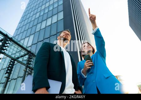 Donna d'affari che indica un collega vicino all'edificio degli uffici Foto Stock