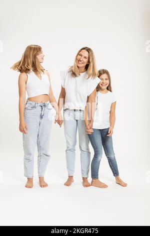 Madre e figlie felici che tengono le mani su sfondo bianco Foto Stock