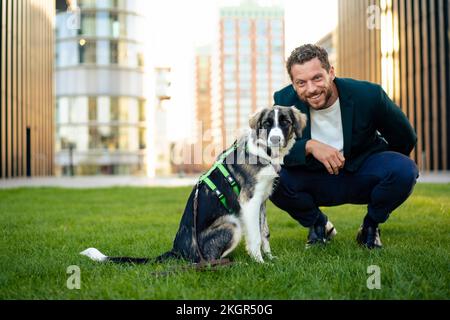 Uomo d'affari sorridente con cane da compagnia accovacciato sull'erba Foto Stock