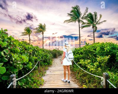 Donna che cammina sul bellissimo Beach Path incorniciato da Palmtrees che conduce alla spiaggia, Hollywood Beach, Sunrise Miami, Florida del Sud, USA Foto Stock