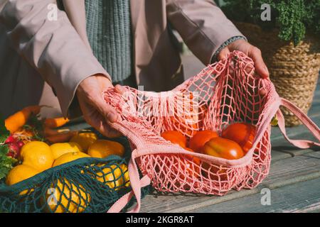 Mani di donna che mostrano pomodori in sacchetto di maglia sul tavolo Foto Stock