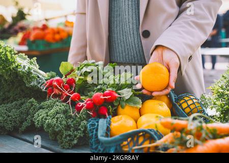 Mano di donna che mostra l'arancio sopra le verdure sul tavolo Foto Stock