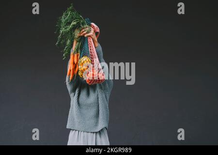 Donna che copre il viso con carote e frutta in sacchi a rete Foto Stock