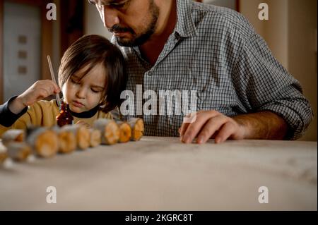 Padre che assiste figlio spazzolando olio su legno Foto Stock