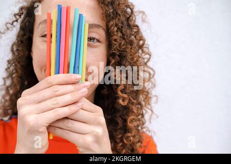 Donna sorridente che tiene matite colorate davanti al viso Foto Stock