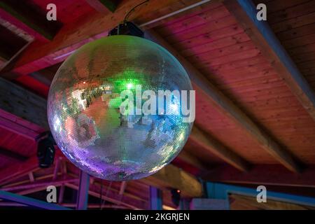 Una grande sfera a specchio da discoteca che riflette luci colorate appese a un soffitto di legno Foto Stock