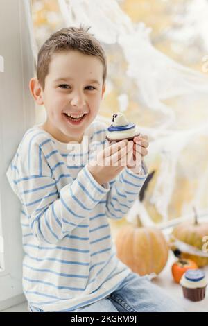 Ragazzo felice con cupcake seduto davanti alla finestra di casa Foto Stock