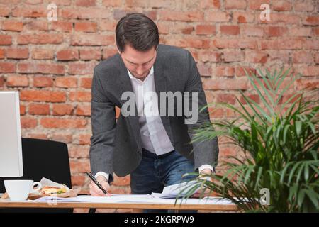 Uomo d'affari che fa la documentazione in piedi dalla scrivania in ufficio Foto Stock