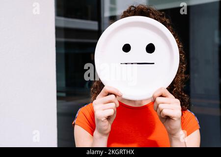 Giovane donna che tiene dritto emoticon piastra sorridente sul viso Foto Stock