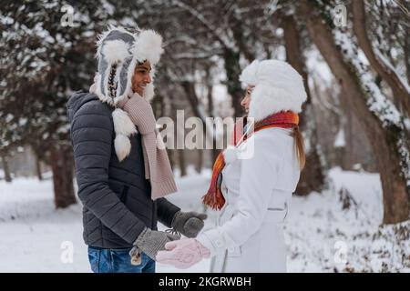 Felice giovane uomo con donna in piedi al parco in inverno Foto Stock