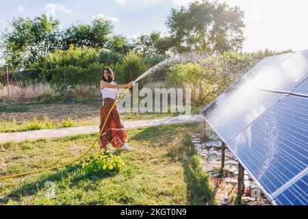 Donna matura che pulisce pannelli solari in cortile nel giorno di sole Foto Stock