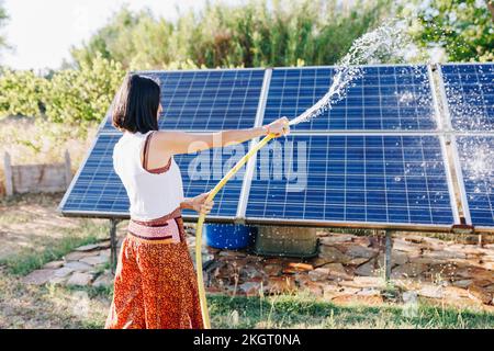 Donna spruzzando acqua e pulendo pannelli solari in giardino Foto Stock