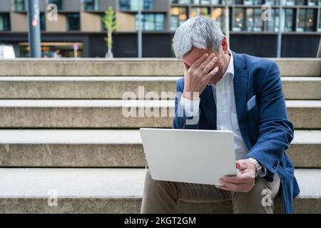 Un uomo d'affari stressato seduto con un computer portatile sulla scala Foto Stock