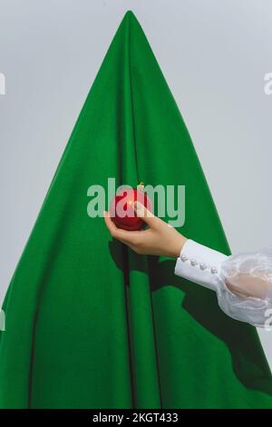 Ragazza adolescente che tiene ornamento rosso di fronte all'albero astratto di Natale Foto Stock