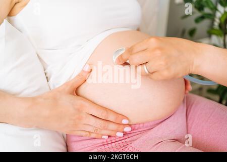 Mano del medico che esamina il ventre di donna incinta con stetoscopio Foto Stock