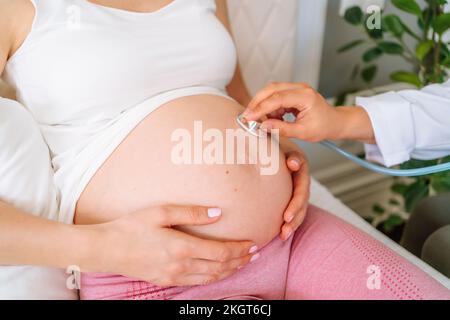 Medico con stetoscopio che esamina la donna incinta a casa Foto Stock