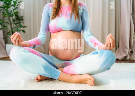 Donna incinta meditando nella posizione del loto a casa Foto Stock