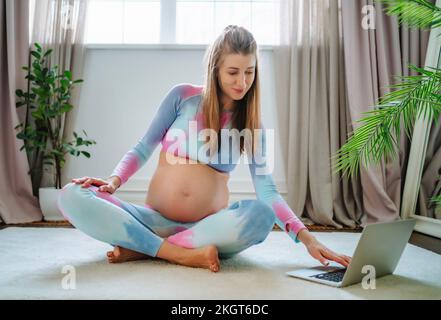 Donna incinta che impara yoga sul computer portatile a casa Foto Stock
