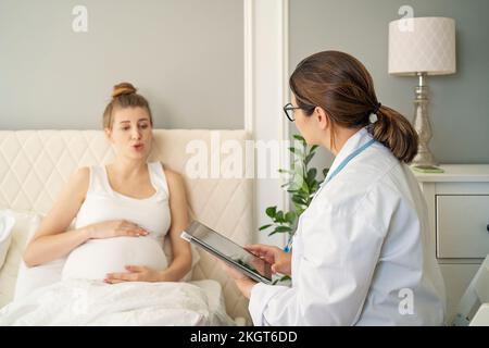Medico che parla con una donna incinta a letto a casa Foto Stock
