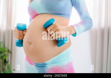 Donna incinta che tiene manubri a casa Foto Stock