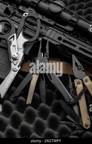 multitool moderno con molti strumenti. Accanto all'arma si trova uno strumento militare portatile multi-tasking. Forbici multifunzione. Sfondo scuro. Foto Stock