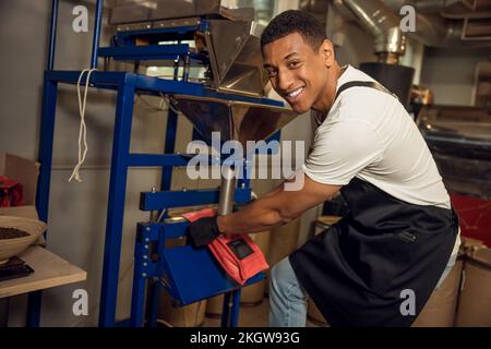 Allegro lavoratore sigillare una borsa da caffè con il termosigillatore Foto Stock