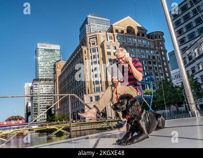 Piccolo-grande uomo d'affari concetto Città posizione con cane fuori sulla chiatta ufficio su smartphone iPhone e controllare iPad computer Canary Wharf Londra E14 Foto Stock