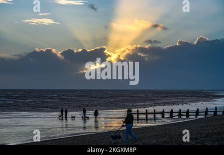 Worthing UK 23rd novembre 2022 - il sole si nasconde dietro le nuvole scure come gli escursionisti del cane godersi una passeggiata nel tardo pomeriggio lungo la spiaggia di Lancing con la bassa marea dopo una giornata di sole e docce pesanti: Credit Simon Dack / Alamy Live News Foto Stock