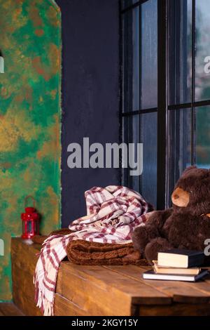 Un posto per rilassarsi vicino alla finestra con una coperta calda, libri e un orsacchiotto Foto Stock