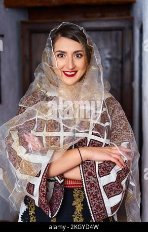 Giovane donna rumena vestita in costume tradizionale popolare, in una casa rurale tradizionale Foto Stock