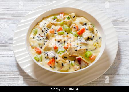 Zuppa cremosa di riso selvatico tacchino con patate rosse. carota, sedano, spezie ed erbe in ciotola bianca su tavolo di legno, vista sul paesaggio Foto Stock